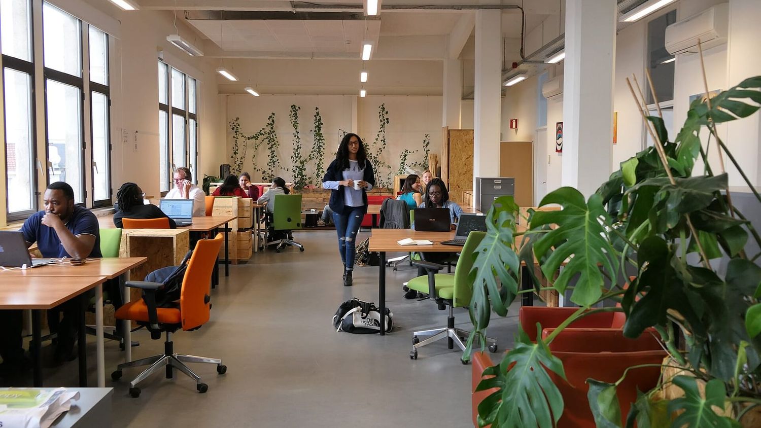 Offener Coworking-Raum mit Holztischen, Laptops und Grünpflanzen, an dem mehrere Leute arbeiten
