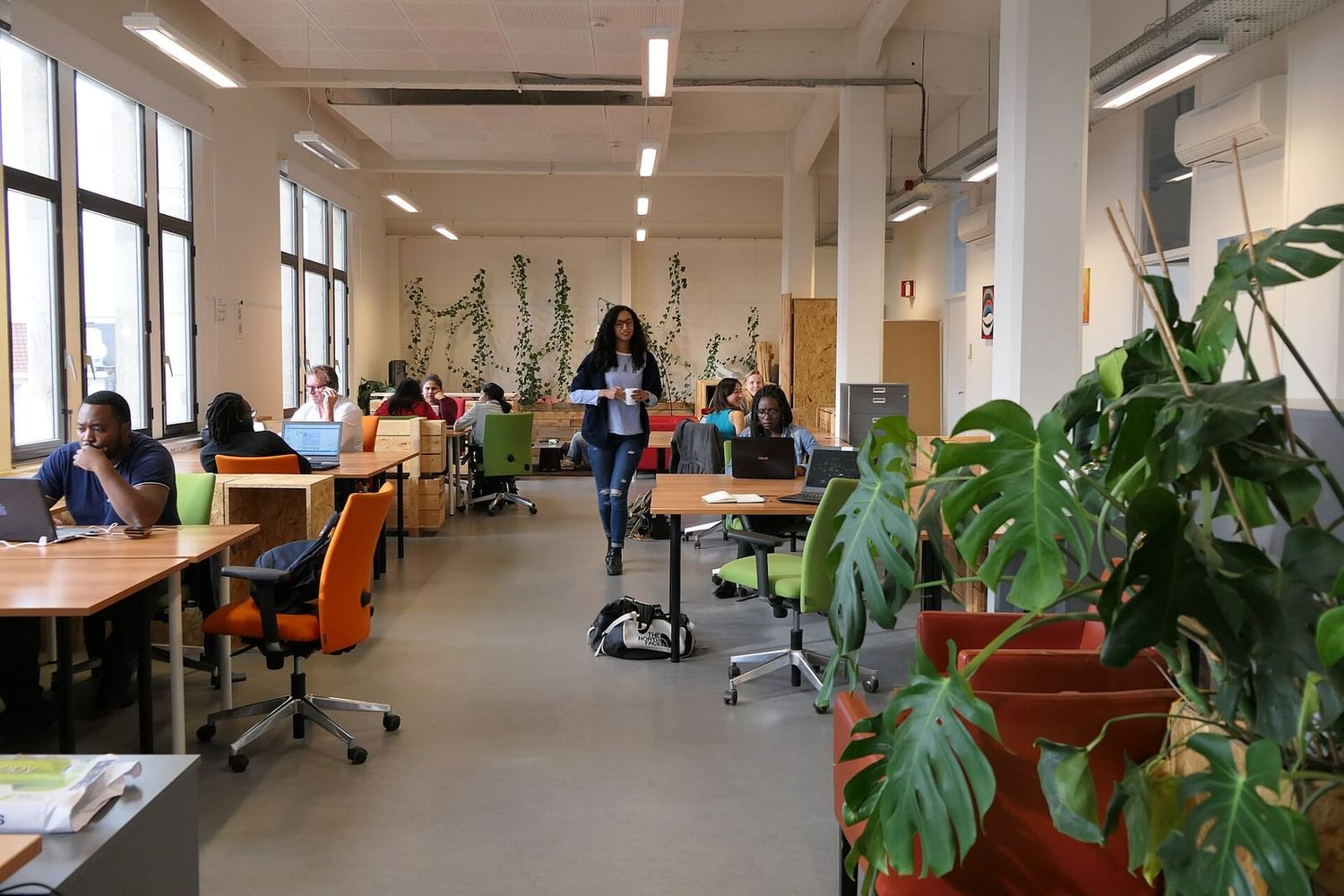 Offener Coworking-Raum mit Holztischen, Laptops und Grünpflanzen, an dem mehrere Leute arbeiten