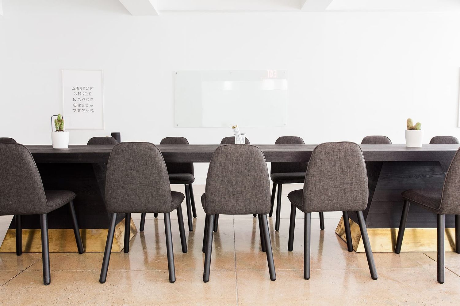 Langer dunkler Konferenztisch mit gepolsterten Stühlen vor weißer Wand mit Glas-Whiteboard