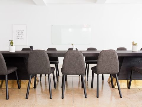 Langer dunkler Konferenztisch mit gepolsterten Stühlen vor weißer Wand mit Glas-Whiteboard
