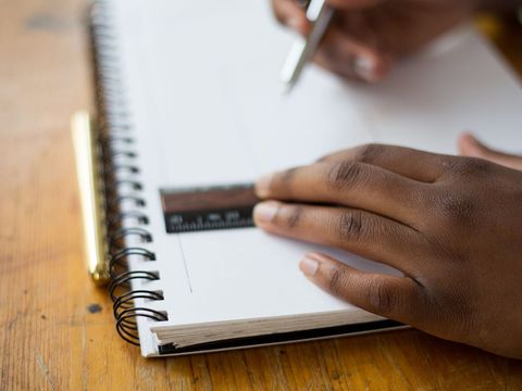 Hände ziehen mit Lineal und Stift eine Linie auf einem Spiralblock am Holztisch