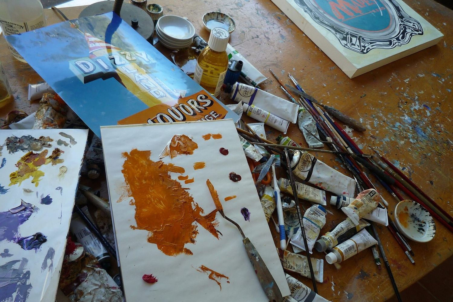 Arbeitstisch eines Schildermalers mit Farbtuben, Pinseln, Palette und halbfertigen Schriftzügen