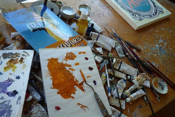 Sign painter's work table with paint tubes, brushes, a palette and unfinished lettering